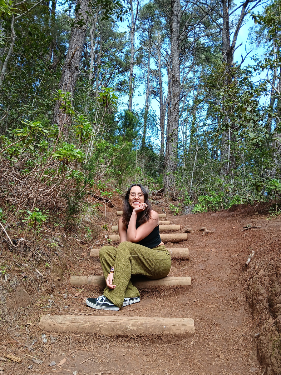 Icíar sonriendo, sentada en una escalera de troncos en el bosque